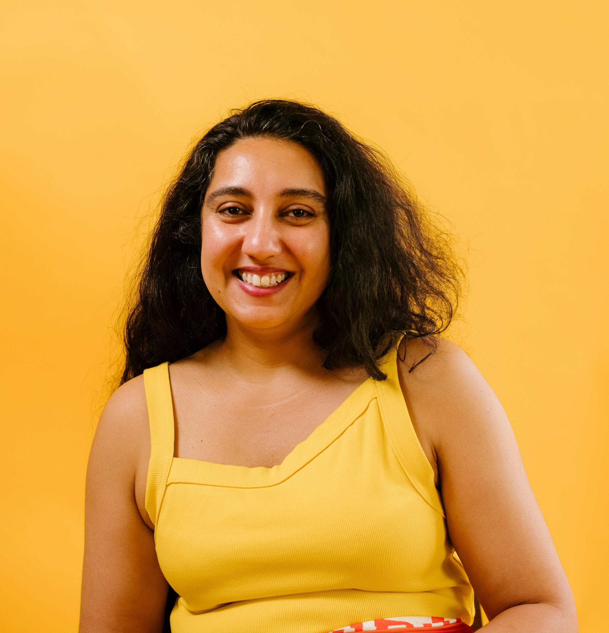 Brown-bodied woman with curly, black hair, wearing yellow top