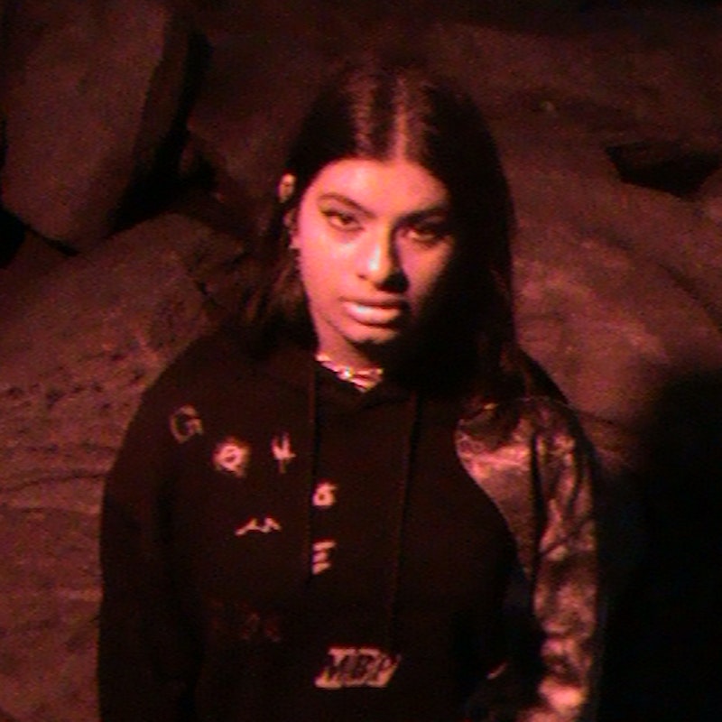 Image of a brown-skinned girl wearing a hoodie and silver jewellery looking up at the camera, with a red light casting upon her.