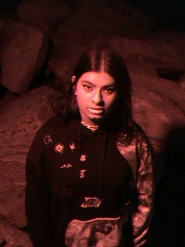Image of a brown-skinned girl wearing a hoodie and silver jewellery looking up at the camera, with a red light casting upon her.