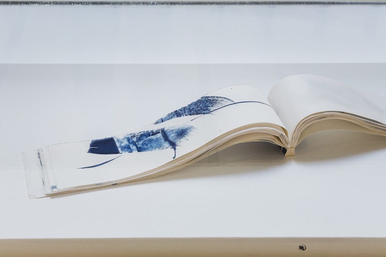 A close-up view of an artist book, flipped open to a page with a dash of blue colour made of cyanotype print