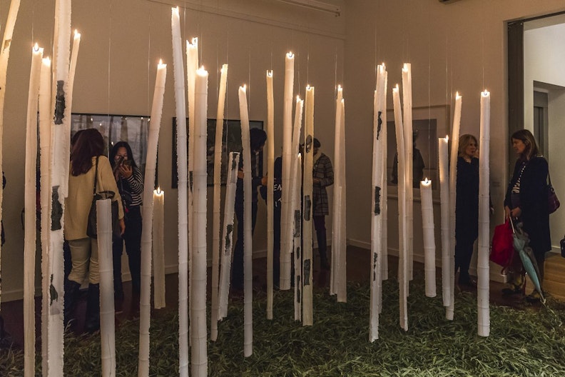 Gallery visitors walk around a sculpture consisting of lit-up wax in bamboo shapes suspended in the gallery