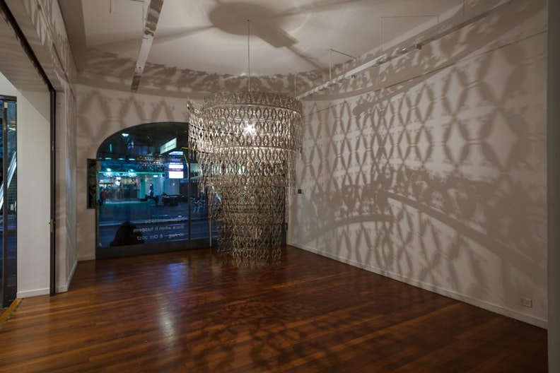 A chandelier is suspended in the middle of a gallery, it casts intricate diamond-shaped patterns on the gallery walls
