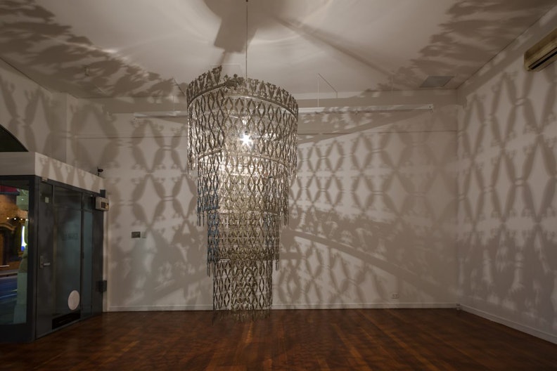 A chandelier is suspended in the middle of a gallery, it casts intricate diamond-shaped patterns on the gallery walls