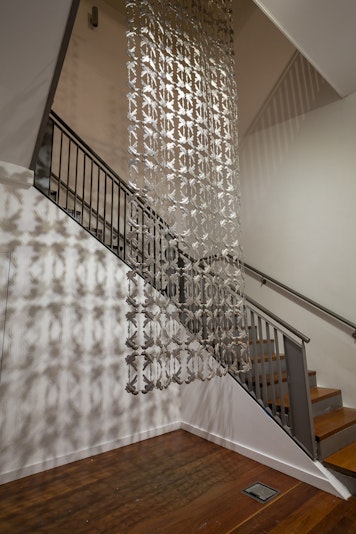 A large sculpture made of intricate metal cutout shapes hangs from above a stairwell