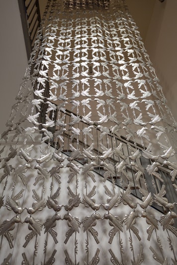 A closer view of a sculpture made of intricate metal cutout shapes birds cascades hangs from the ceiling