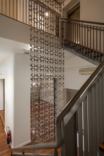 A large sculpture made of intricate metal cutout shapes birds hangs from the ceiling against a stairwell