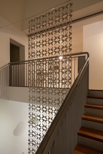 A sculpture made of intricate metal cutout shapes birds cascades hangs from the ceiling on top of a stairwell on the second floor