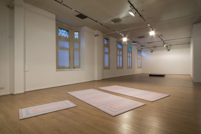 Three prayer mats arranged on the gallery floor, two of them are parellel to each other while a smaller one lays perpendicular to them