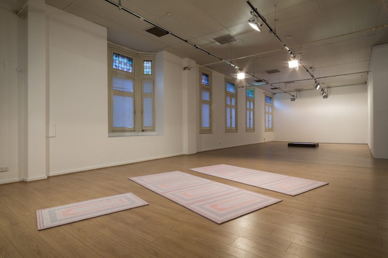 Three prayer mats arranged on the gallery floor, two of them are parellel to each other while a smaller one lays perpendicular to them