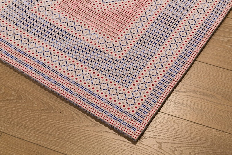 A close-up of a corner of a prayer mat, showing intricate geometric patterns made of hundreds of playing die