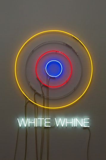 A multi-coloured neon light in the shape of a target has the neon text 'WHITE WHINE' underneath