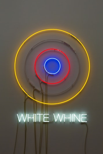 A multi-coloured neon light in the shape of a target has the neon text 'WHITE WHINE' underneath