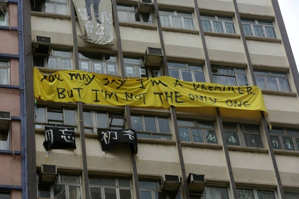 A yellow banner that reads 'You may say I'm a dreamer but I'm not the only one' on an apartment block complex.