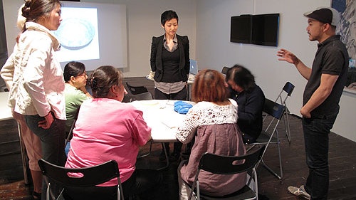 A group sits at a table during Liyen Chong's Threaded Stories Workshop and listens to a speaker