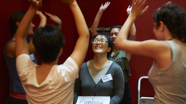 People standing around Eunhye Hwang in a circle with their hands raised during a performance of It Without a Blink