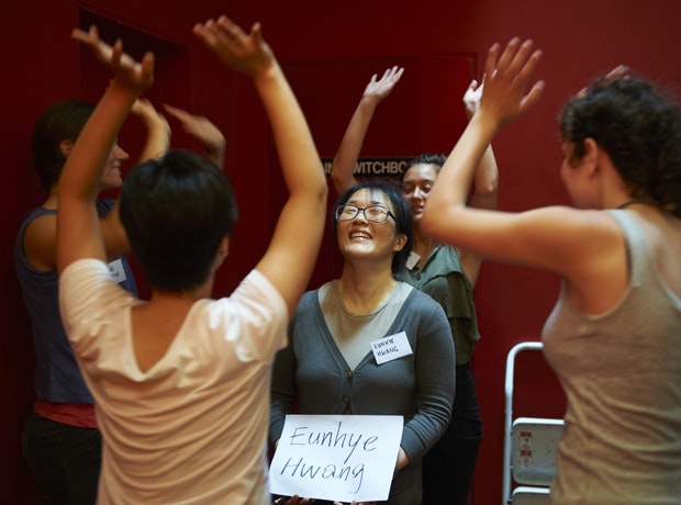 People standing around Eunhye Hwang in a circle with their hands raised during a performance of It Without a Blink