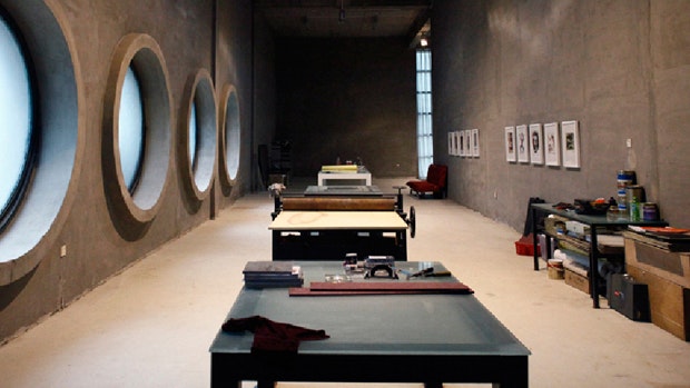 A photo showing a room with concrete walls, tables, and round windows inside Shen Shaomin Studios, Beijing