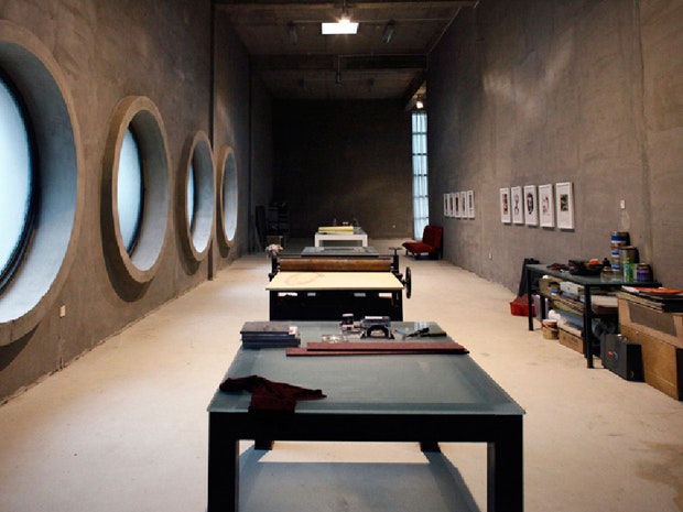 A photo showing a room with concrete walls, tables, and round windows inside Shen Shaomin Studios, Beijing