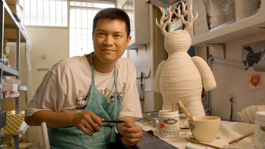 A photo of Vipoo Srivilasa sitting at a workshop table with a sculpture