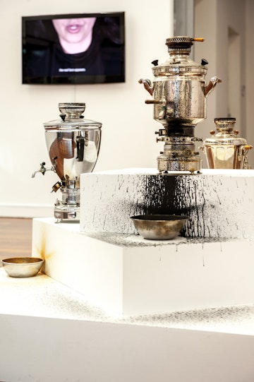 Front: Nasim Nasr, Slow Burn (2013), Samovars, ink, oil, tea; dimensions variable.Installation view, 4A Centre for Contemporary Art. Courtesy the artist and GAGPROJECTS, Adelaide/Berlin.  Back: Nasim Nasr, Ashob: Unrest (2015), single-channel video, sound, subtitles. Installation view, 4A Centre for Contemporary Art. Courtesy the artist and GAGPROJECTS Adelaide/Berlin. This work was produced with assistance from 4A Centre for Contemporary Asian Art. Image: Justin Malinowski