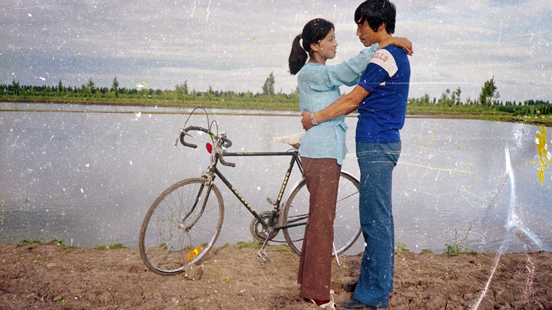 An image from Beijing Silvermine, showing two Chinese people standing next to a bicycle near a river
