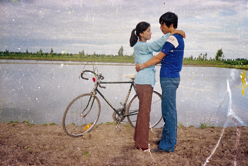 An image from Beijing Silvermine, showing two Chinese people standing next to a bicycle near a river