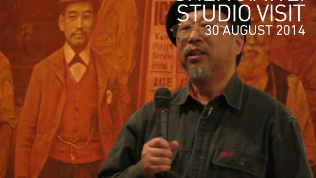 A photo of Shen Jiawei holding a microphone standing in front of his artwork