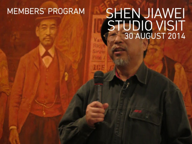 A photo of Shen Jiawei holding a microphone standing in front of his artwork