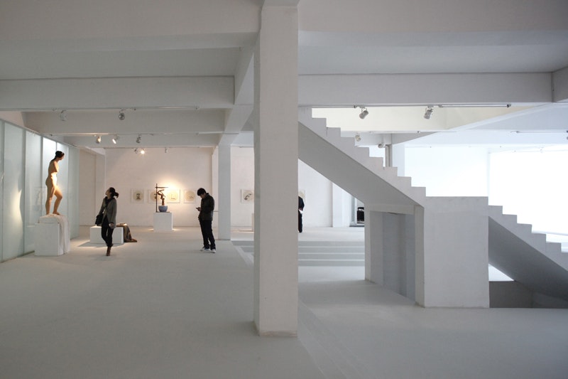The white interior of an art gallery with a staircase and two people examining artworks