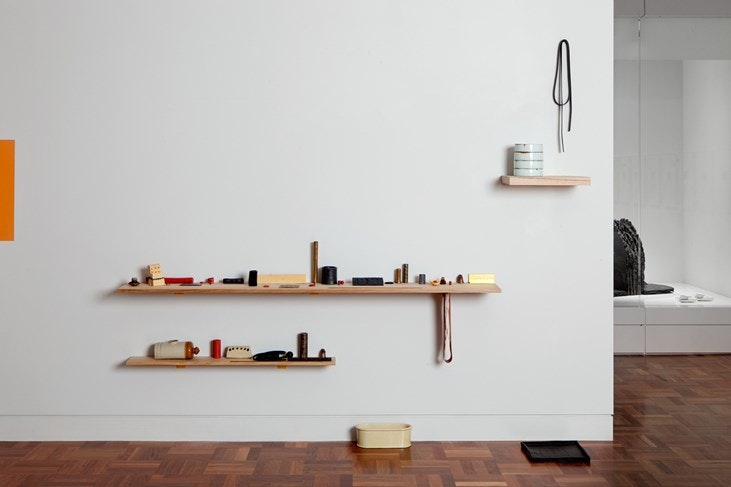 A white wall inside an art gallery, shelves with assorted artworks