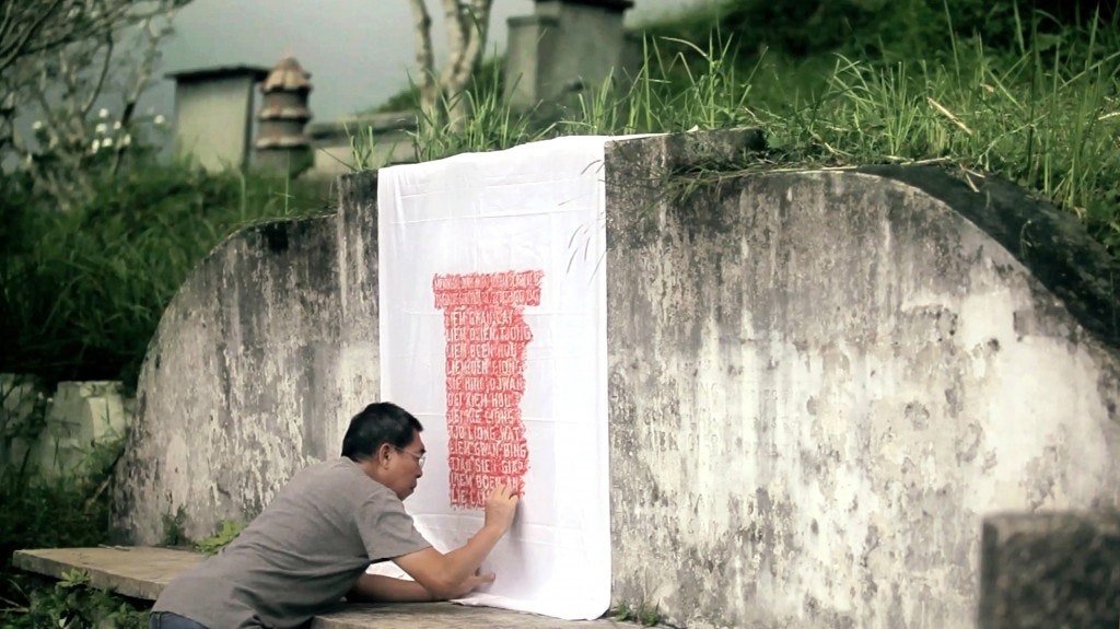 A screenshot from the film Pilgrimage, depicting an artist working on a white sheet outdoors