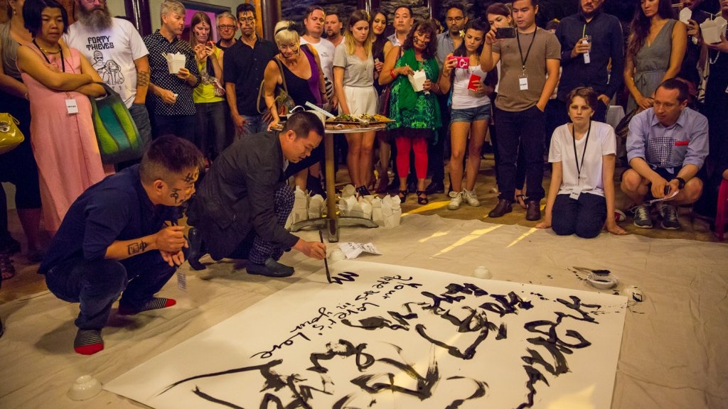 A photo of two artists creating shu fa (Chinese calligraphy) on a sheet with a large crowd gathered watching at night