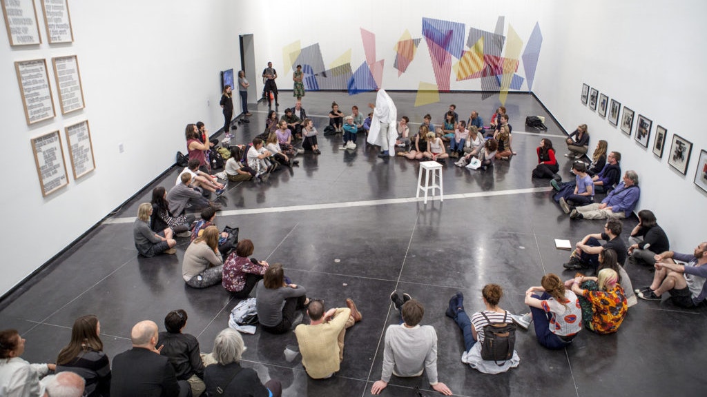 A photo of Brian Fuata's performance of Untitled (ghost machinery refit / letting go of the sheet – a possible addition to a program of events) at Chisenhale Gallery, with the audience sitting in a circle