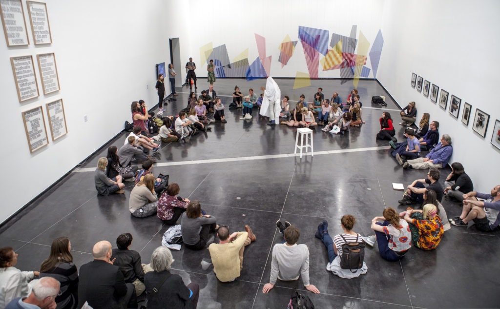 A photo of Brian Fuata's performance of Untitled (ghost machinery refit / letting go of the sheet – a possible addition to a program of events) at Chisenhale Gallery, with the audience sitting in a circle