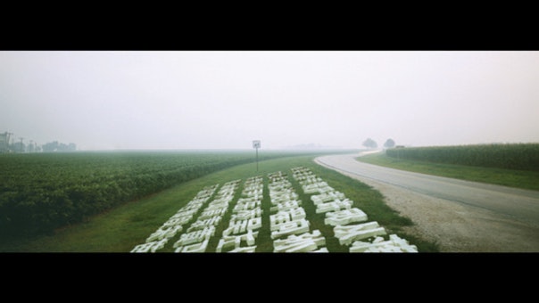 A video still depicting white Chinese characters next to a road and a green field in the countryside