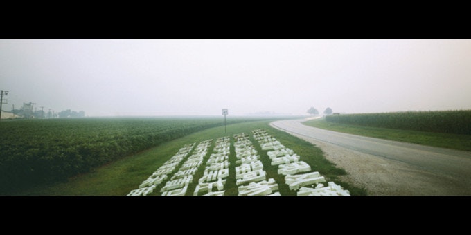 A video still depicting white Chinese characters next to a road and a green field in the countryside