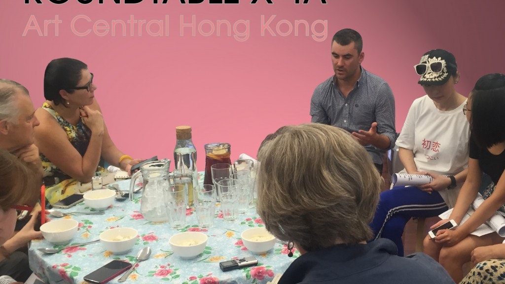 A group of people sitting and discussing around a table with a pink background