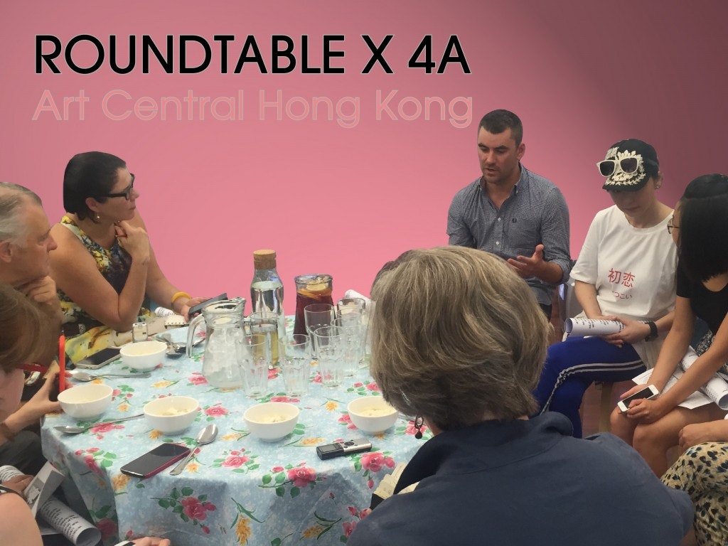 A group of people sitting and discussing around a table with a pink background