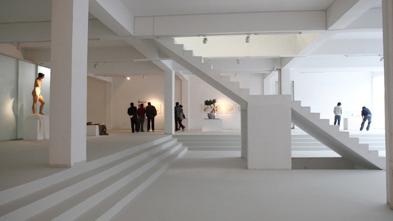 The white interior of a studio gallery, white steps and staircase, people viewing artwork against the far wall