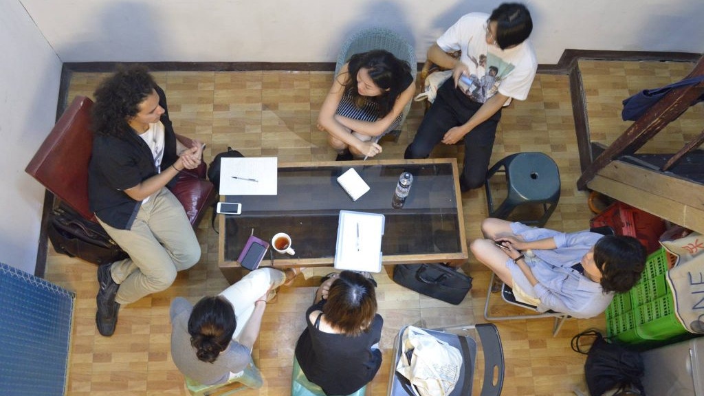 An overhead photo of a group sitting around a glass table in discussion