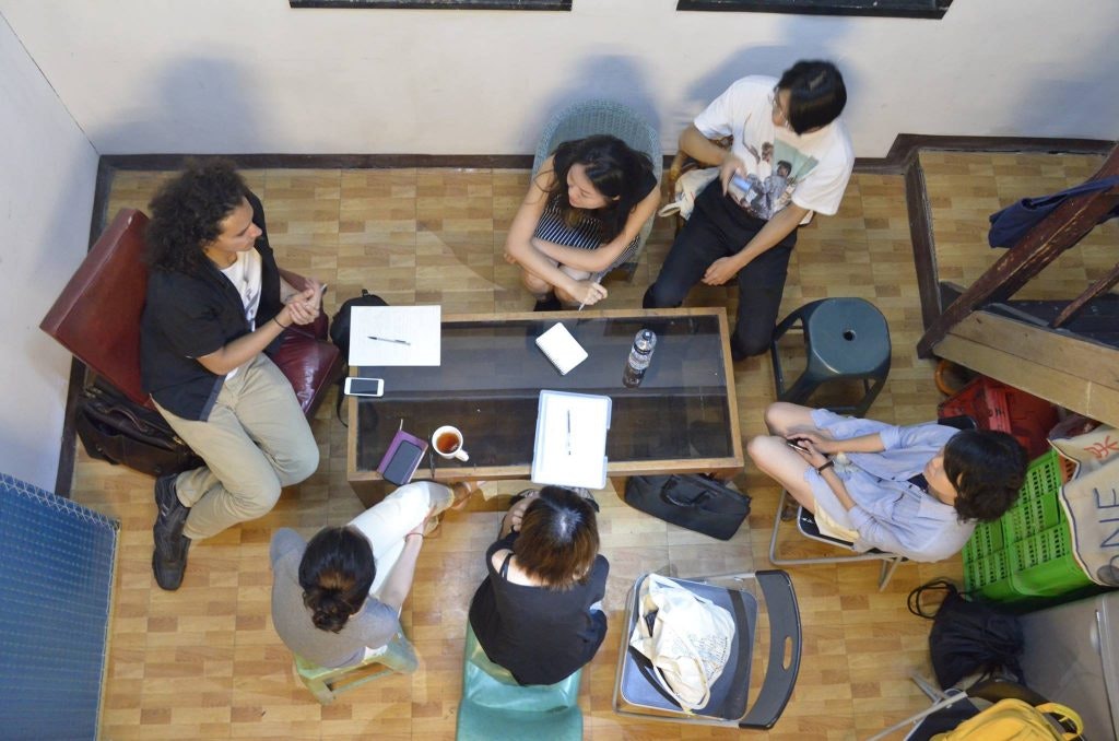 An overhead photo of a group sitting around a glass table in discussion