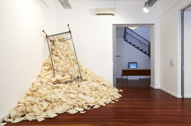 Front: Araya Rasdjarmrearnsook, Has Girl Lost her Memory (first created 1994, 2014 iteration), corn husks and bed frame; installation view, 4A Centre for Contemporary Asian Art. Courtesy Araya Rasdjarmrearnsook.  Back: Araya Rasdjarmrearnsook, The Class (2005), single-channel video; installation view, 4A Centre for Contemporary Asian Art. Courtesy Araya Rasdjarmrearnsook. Photo: Zan Wimberley