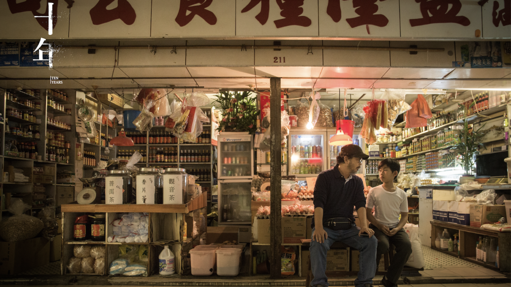 An image still from the film "Ten Years" showing a man and child seated outside a Hong Kong convenience store