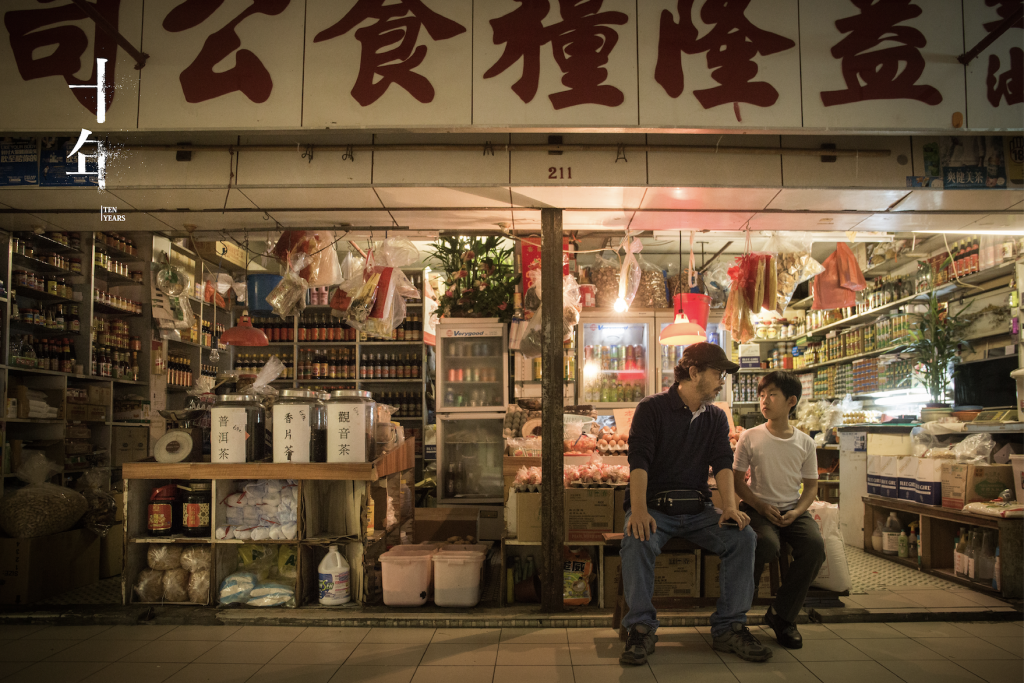 An image still from the film "Ten Years" showing a man and child seated outside a Hong Kong convenience store