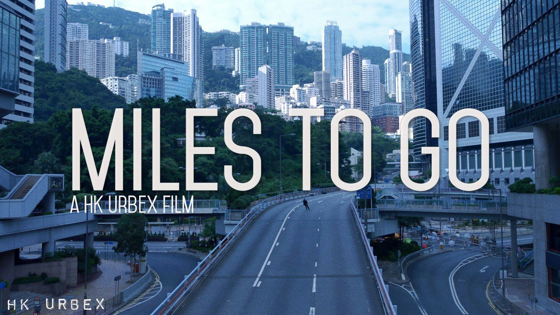 An image still from the short film "Miles to Go" showing a Hong Kong street with apartment blocks on hills