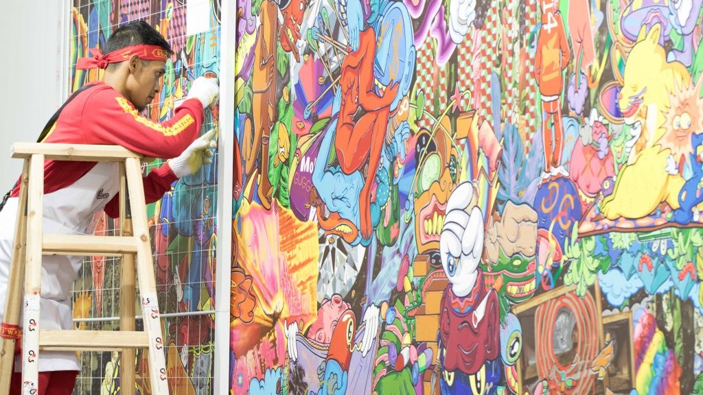 A photo of Hahan standing on a ladder installing his artwork on a wall