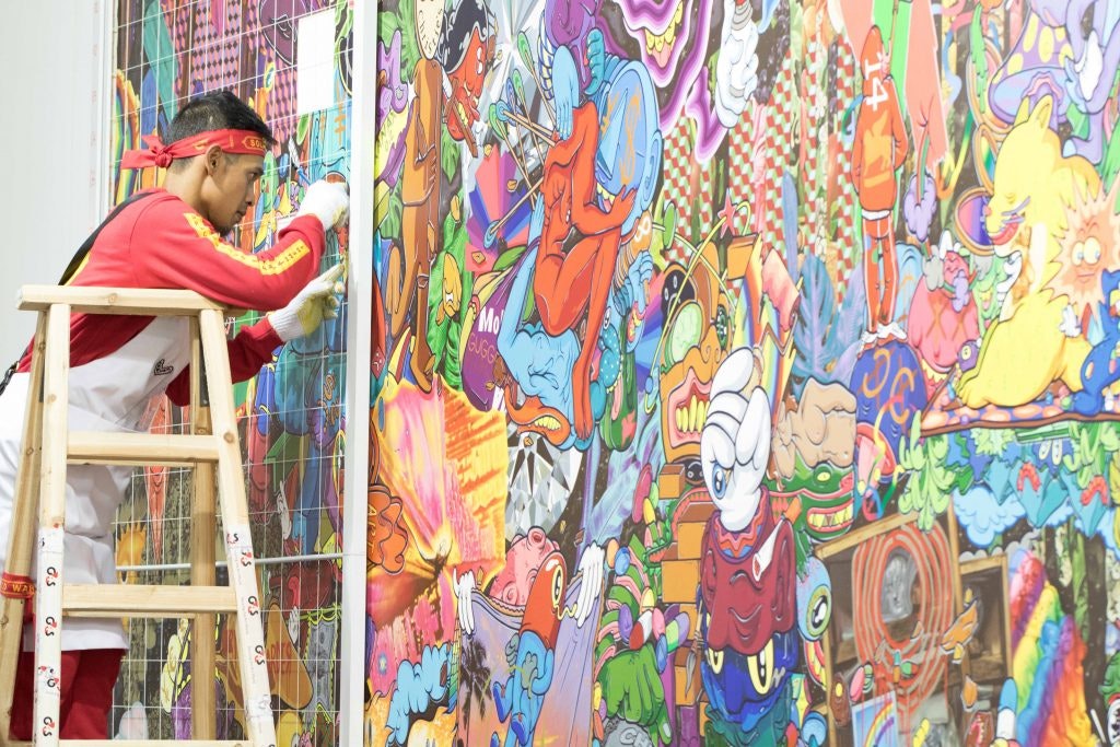 A photo of Hahan standing on a ladder installing his artwork on a wall