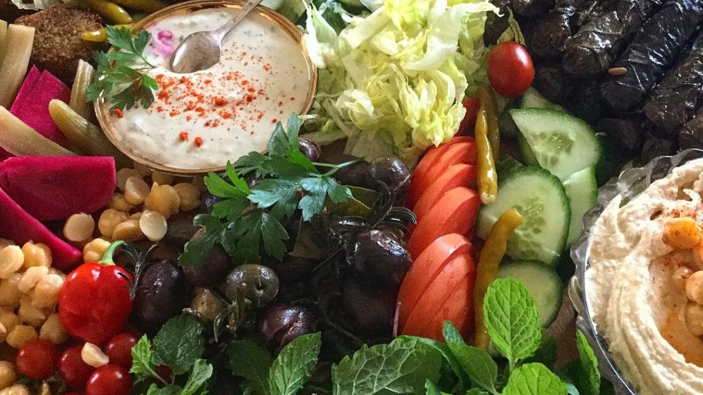 A photo of Lebanese food, including colourful vegetables, falafel, and hummus.