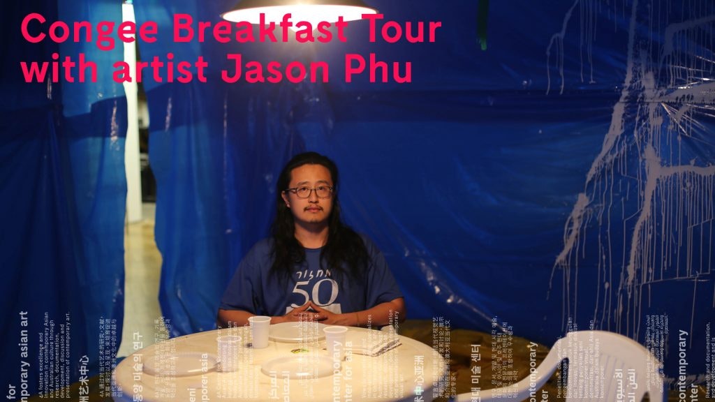Photo of artist Jason Phu seated at a white table with blue curtains behind him.