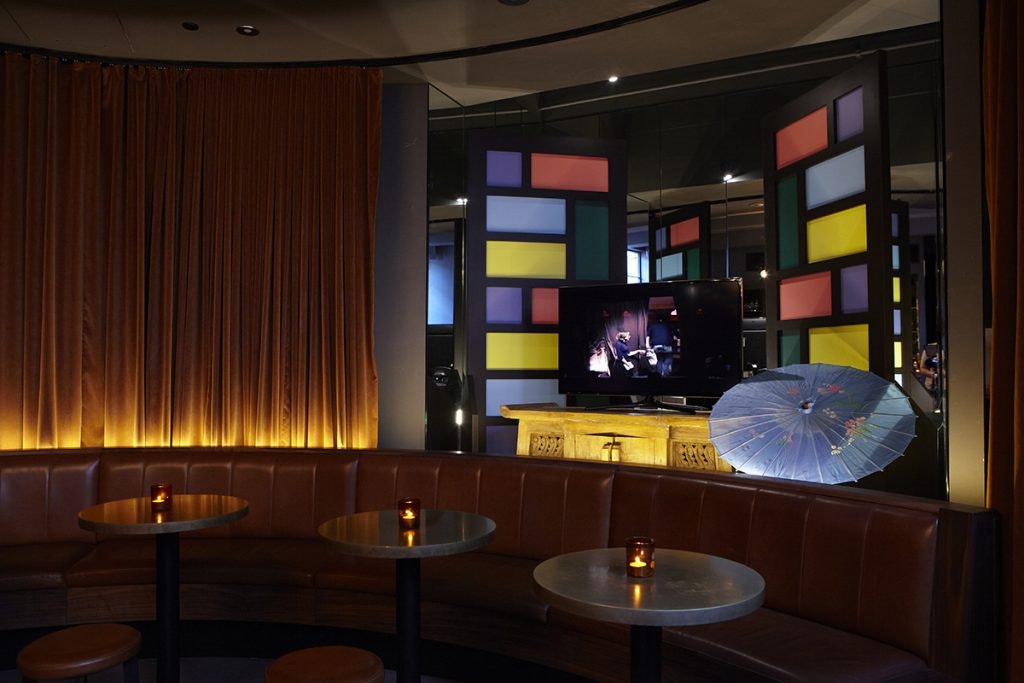 Inside Golden Age Cinema and Bar, tables, booths, golden curtains, and a TV monitor
